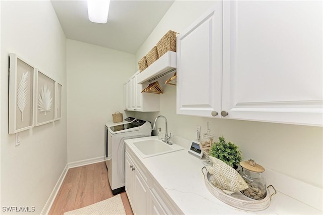 washroom featuring baseboards, light wood-style flooring, cabinet space, a sink, and washing machine and dryer