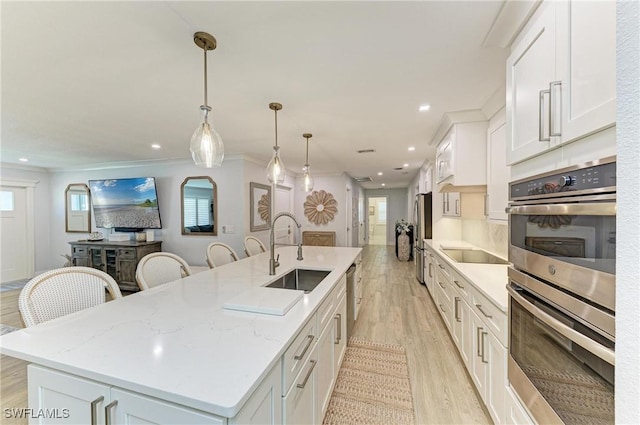 621 Trabue Ave, Punta Gorda, FL 33950 - kitchen with stainless steel appliances, a center island with sink, a sink, light wood finished floors, and white cabinets