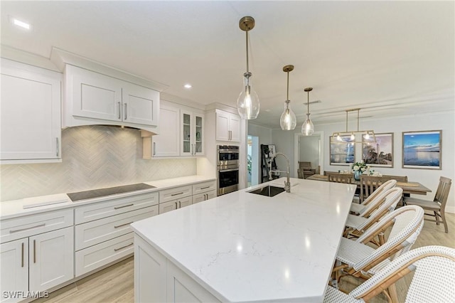 621 Trabue Ave, Punta Gorda, FL 33950 - kitchen with an island with sink, a sink, stainless steel double oven, black electric cooktop, and white cabinets