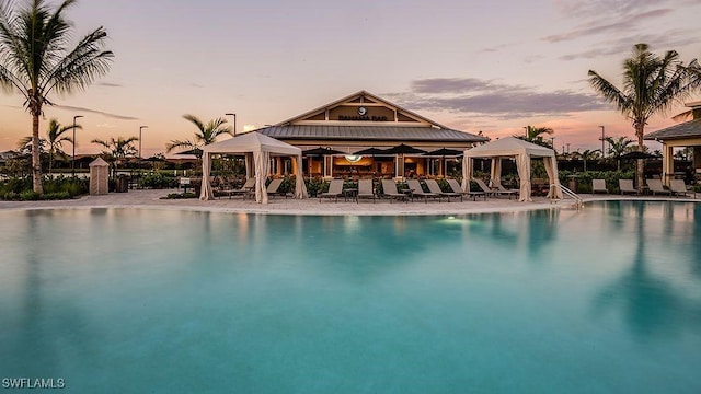 pool at dusk featuring a patio area, a gazebo, and a community pool