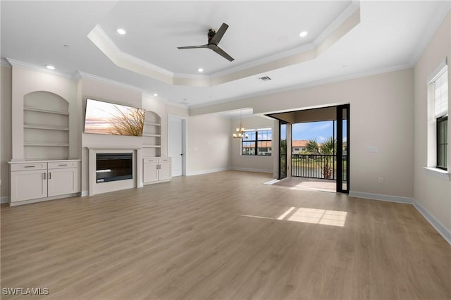 unfurnished living room featuring built in features, a tray ceiling, light wood-style flooring, and a glass covered fireplace