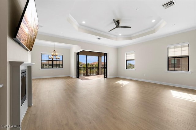 unfurnished living room with a tray ceiling, ceiling fan with notable chandelier, visible vents, and light wood-type flooring