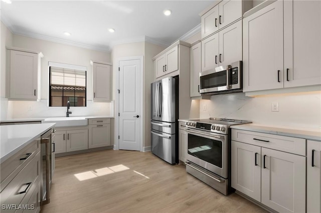 kitchen with a sink, crown molding, light countertops, and appliances with stainless steel finishes