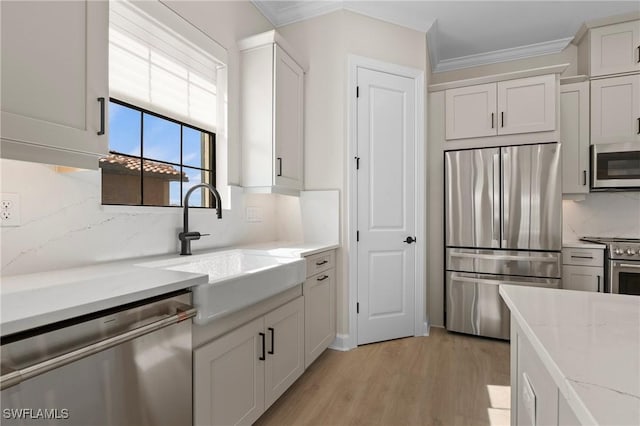 kitchen featuring light wood-style flooring, ornamental molding, tasteful backsplash, appliances with stainless steel finishes, and a sink