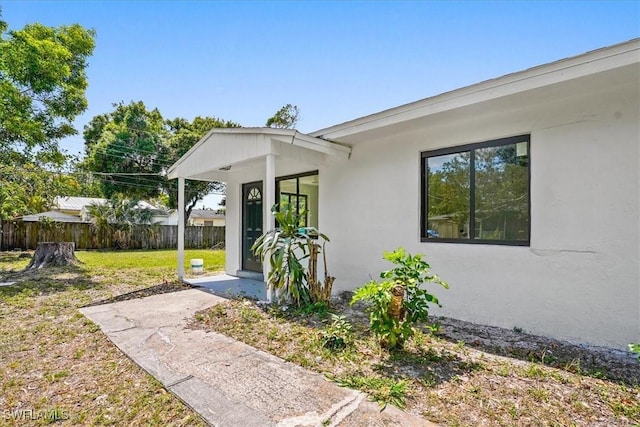 3652 Hibiscus Ave, Naples, FL 34104 - doorway to property with stucco siding, a lawn, and fence