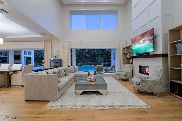 living room with a tray ceiling, visible vents, wood finished floors, and a warm lit fireplace