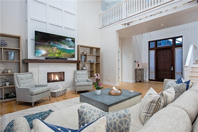 living area with wood finished floors, stairs, a warm lit fireplace, baseboards, and a towering ceiling