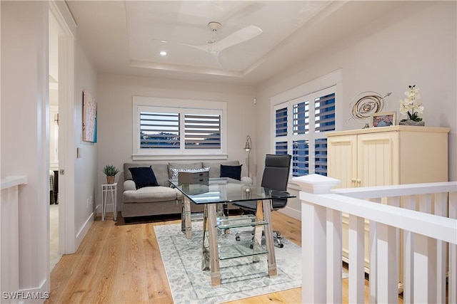 office space with light wood finished floors, a ceiling fan, baseboards, and a tray ceiling