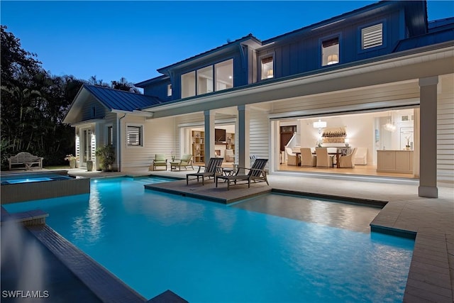rear view of property featuring metal roof, a standing seam roof, a pool with connected hot tub, and a patio area