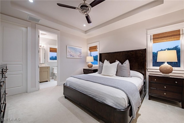 bedroom featuring recessed lighting, light colored carpet, ensuite bathroom, baseboards, and a raised ceiling