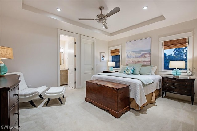 bedroom with recessed lighting, a raised ceiling, light carpet, and ensuite bathroom
