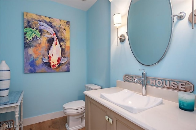 half bath with wood finished floors, toilet, vanity, and baseboards
