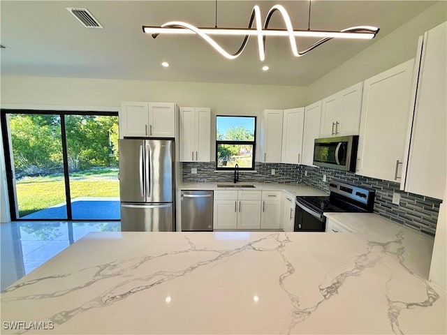 kitchen with visible vents, light stone counters, decorative backsplash, appliances with stainless steel finishes, and a sink