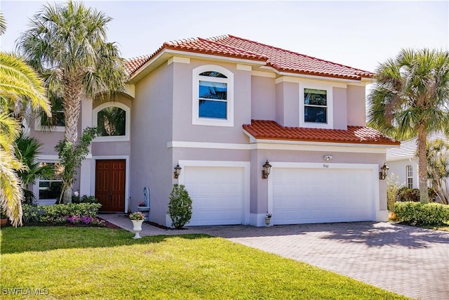 mediterranean / spanish-style home featuring stucco siding, driveway, a front lawn, a tile roof, and an attached garage