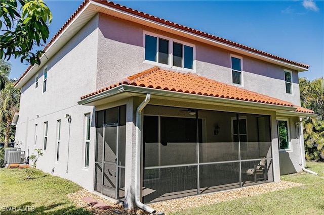 back of property with a tile roof, stucco siding, central AC unit, a lawn, and a sunroom