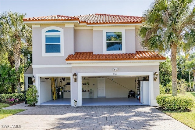 mediterranean / spanish-style house with decorative driveway, a garage, stucco siding, and a tiled roof