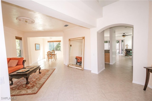hall featuring visible vents, arched walkways, crown molding, light tile patterned floors, and baseboards