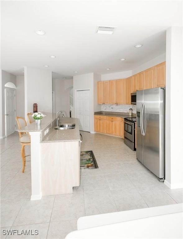 kitchen featuring a sink, a breakfast bar, light brown cabinetry, and stainless steel appliances