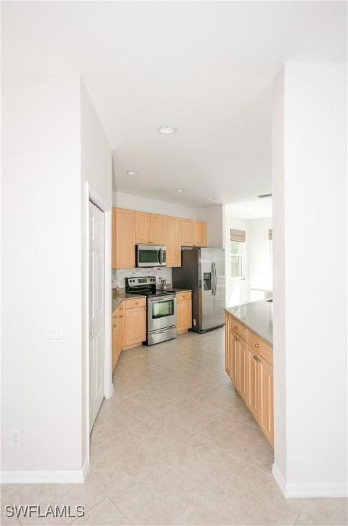 kitchen with decorative backsplash, baseboards, light brown cabinetry, and stainless steel appliances