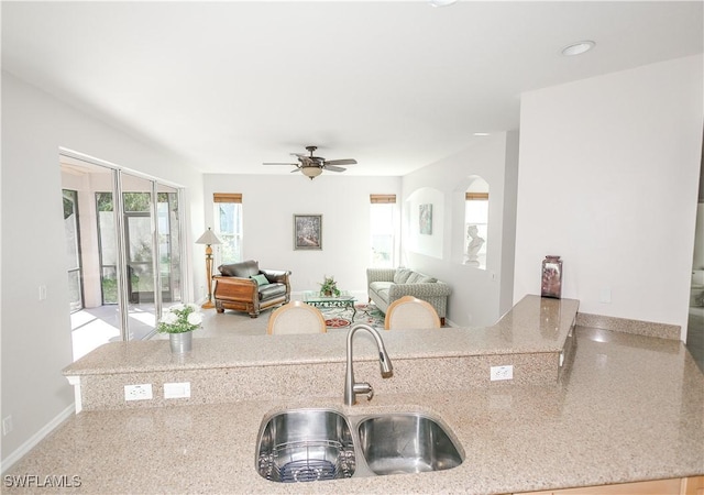 kitchen featuring a sink, open floor plan, baseboards, ceiling fan, and light stone countertops