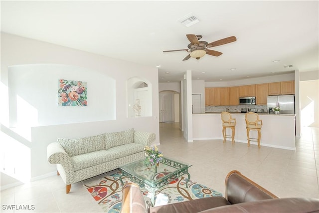 living area featuring light tile patterned floors, a ceiling fan, baseboards, visible vents, and arched walkways