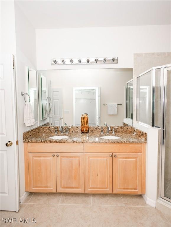 bathroom with tile patterned floors, a shower stall, double vanity, and a sink