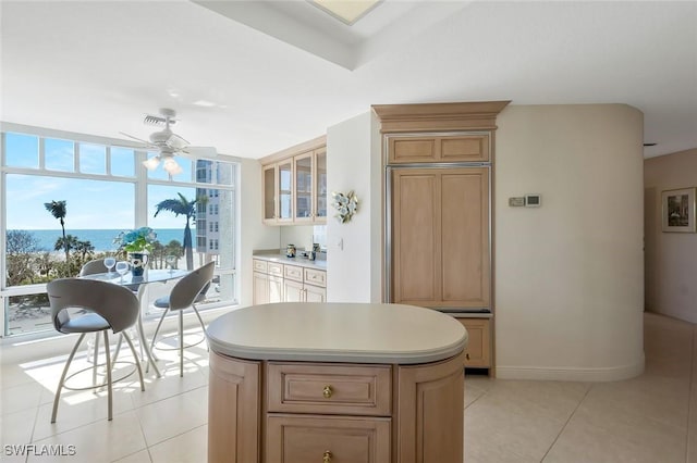 kitchen with light tile patterned floors, a ceiling fan, paneled built in fridge, light countertops, and a center island