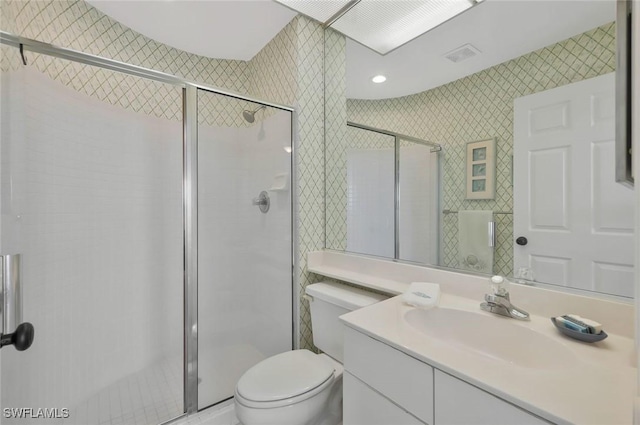 bathroom featuring vanity, visible vents, wallpapered walls, a shower stall, and toilet