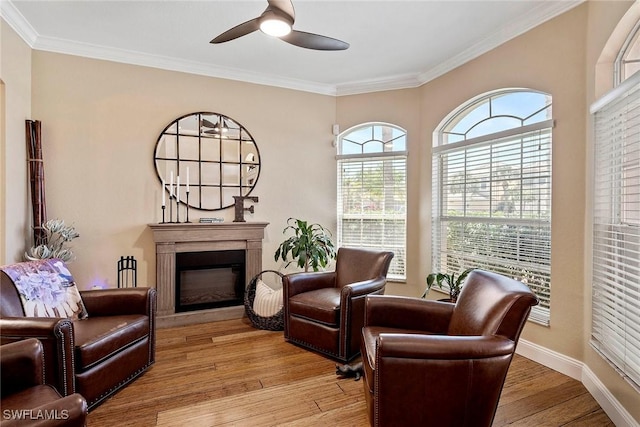 living area featuring ornamental molding, a fireplace, ceiling fan, and light wood-style floors