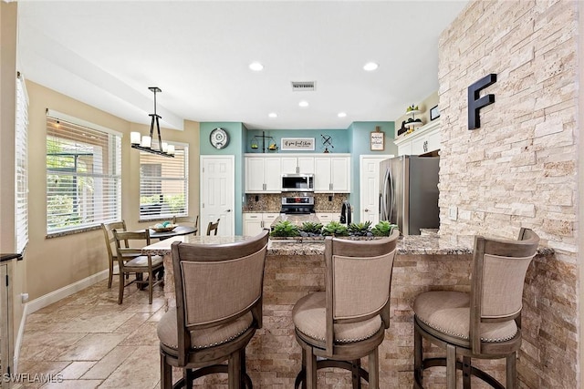 kitchen with white cabinets, visible vents, stainless steel appliances, baseboards, and a peninsula