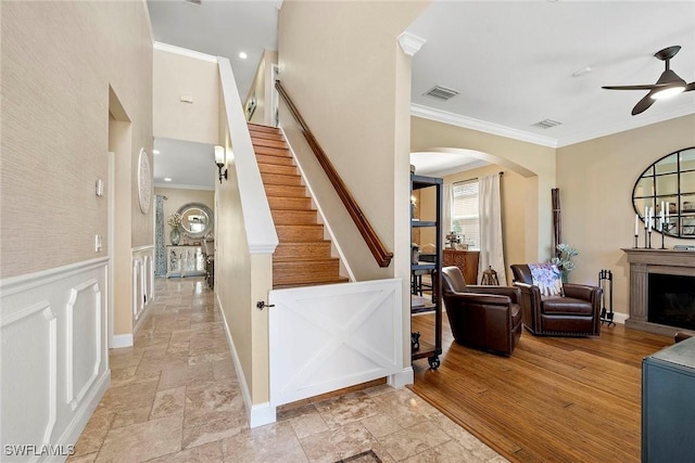 foyer entrance with stone tile floors, crown molding, a ceiling fan, visible vents, and arched walkways