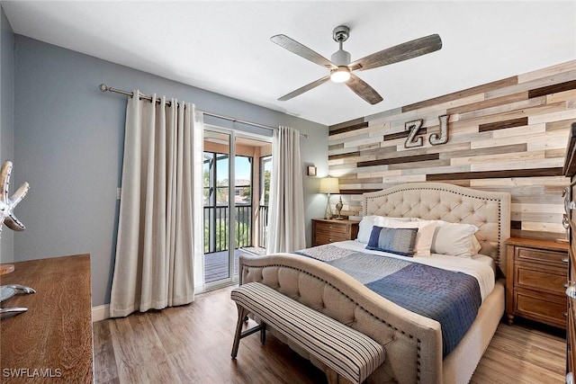 bedroom with wooden walls, an accent wall, wood finished floors, and access to outside