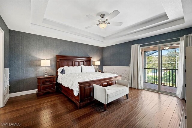 bedroom with wallpapered walls, hardwood / wood-style flooring, access to exterior, ceiling fan, and a tray ceiling