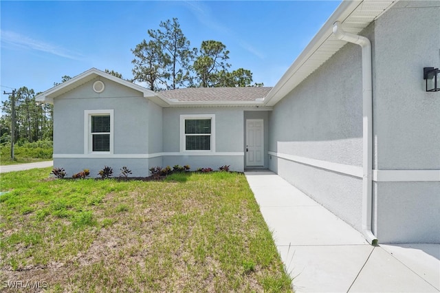 3906 E 10th St, Lehigh Acres, FL 33972 - view of front of house with stucco siding, a front lawn, and a shingled roof