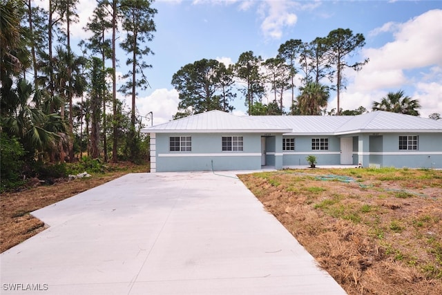 single story home with stucco siding, driveway, and metal roof