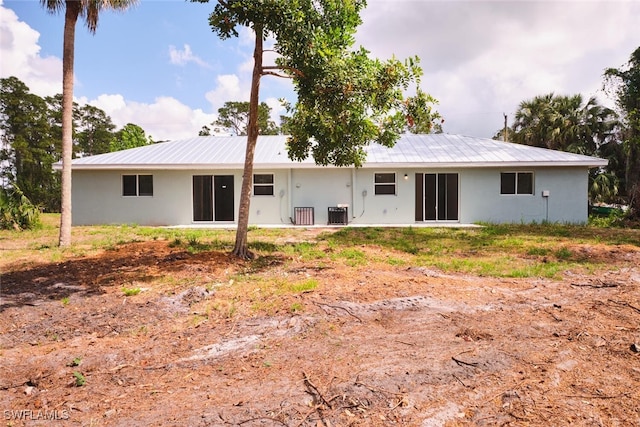 rear view of property featuring central air condition unit, stucco siding, and metal roof