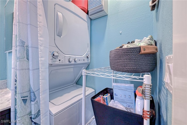 laundry room featuring stacked washer / drying machine and a textured wall