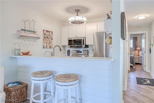 kitchen with a sink, wood finished floors, white cabinetry, a peninsula, and appliances with stainless steel finishes