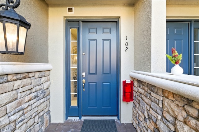 doorway to property featuring visible vents, stucco siding, and stone siding
