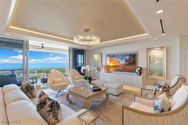 living room with a tray ceiling, a textured ceiling, and ceiling fan with notable chandelier