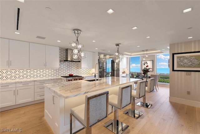 kitchen featuring backsplash, white cabinets, wall chimney range hood, and a sink