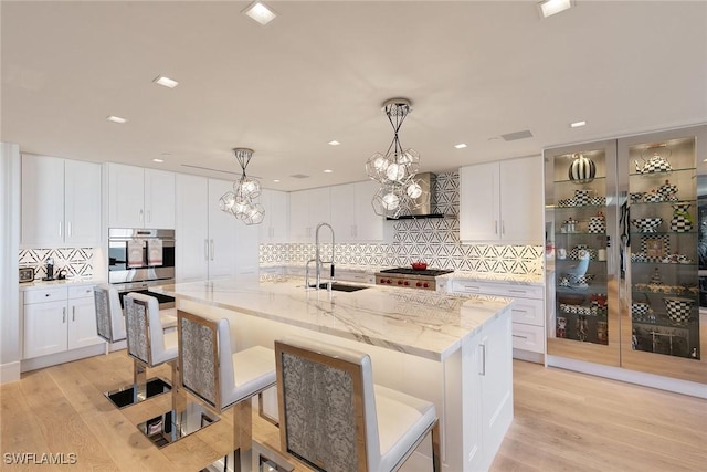 kitchen featuring light wood finished floors, a notable chandelier, white cabinetry, and a sink