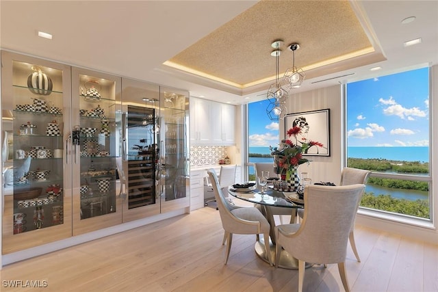 dining room featuring a tray ceiling, a water view, and light wood finished floors