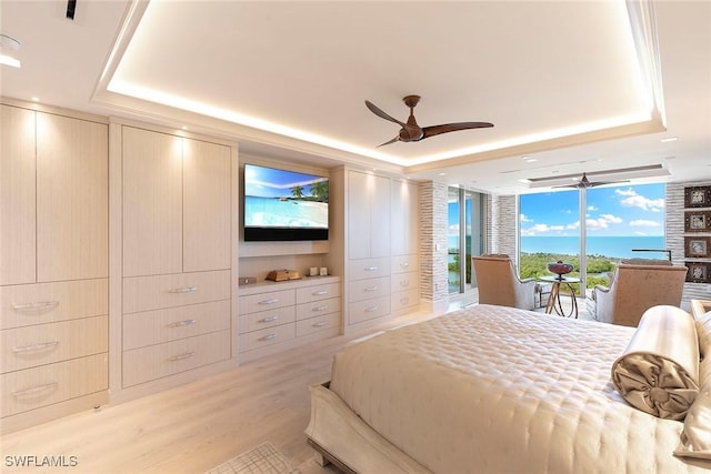 bedroom featuring ceiling fan, a tray ceiling, light wood-style flooring, and access to exterior