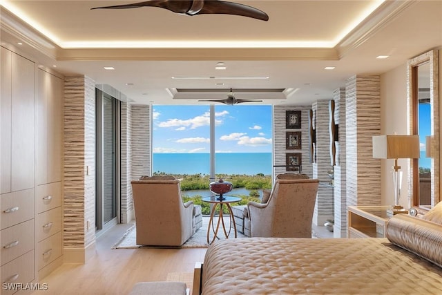 bedroom featuring a tray ceiling, a water view, wood finished floors, and floor to ceiling windows