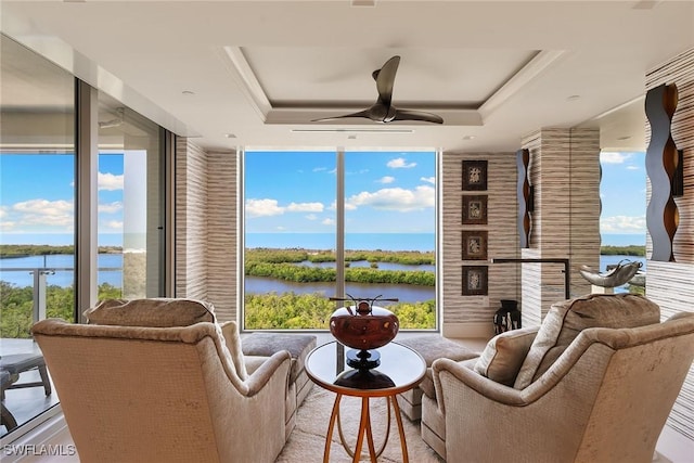 living area with a tray ceiling, a water view, and ceiling fan