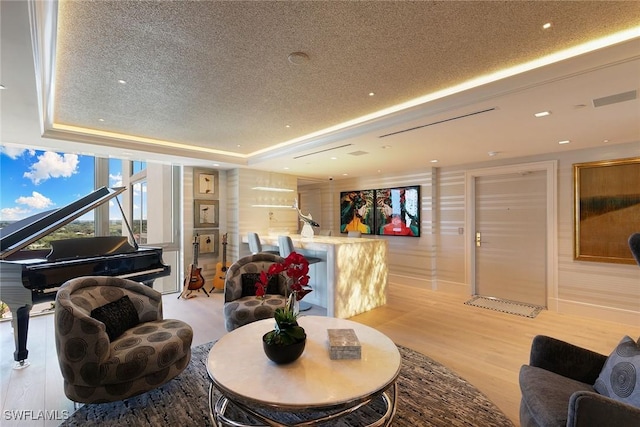living room featuring light wood-style flooring, a textured ceiling, and a raised ceiling