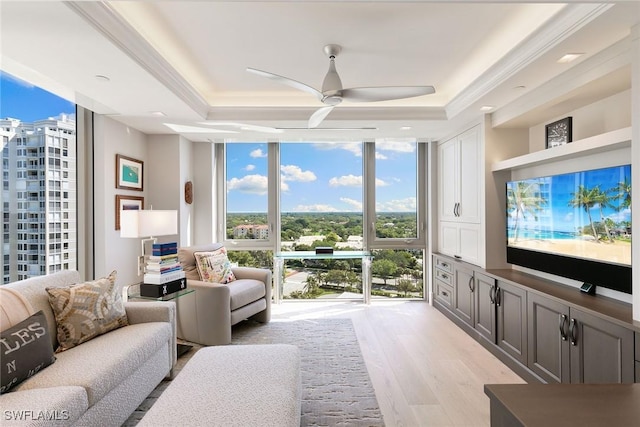 living area featuring crown molding, a tray ceiling, expansive windows, light wood-style flooring, and a ceiling fan