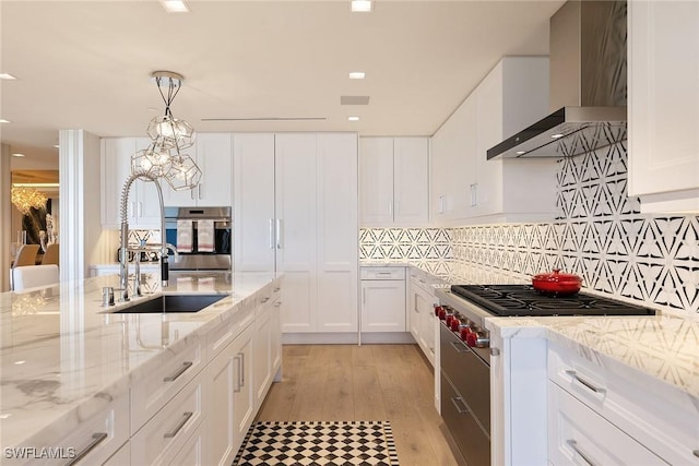 kitchen featuring oven, white cabinets, wall chimney exhaust hood, backsplash, and a chandelier