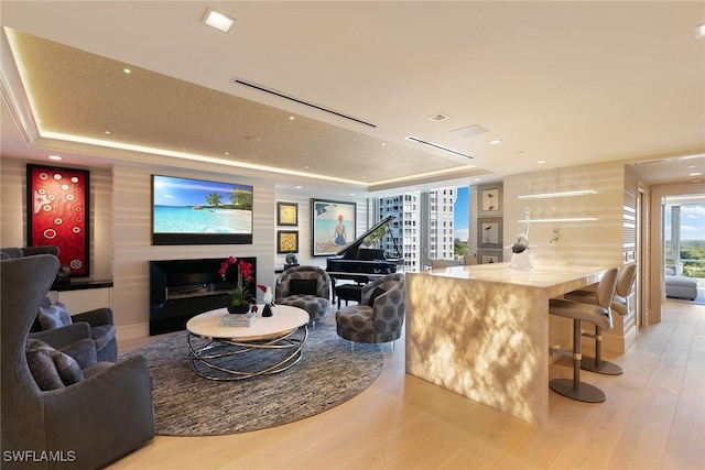 living room with a fireplace, a raised ceiling, and wood finished floors